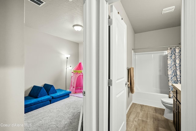 bathroom featuring a textured ceiling, toilet, wood finished floors, vanity, and shower / bath combo