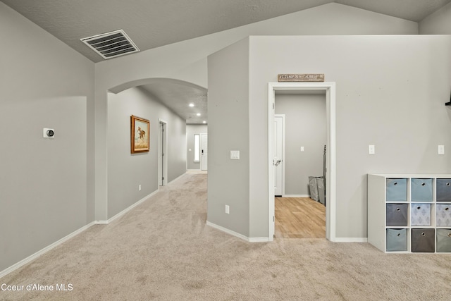 hall with arched walkways, carpet flooring, visible vents, baseboards, and vaulted ceiling