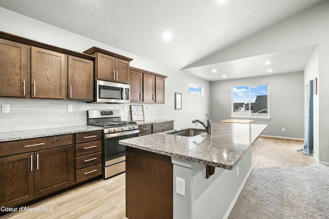 kitchen featuring stainless steel appliances, a sink, vaulted ceiling, backsplash, and light stone countertops