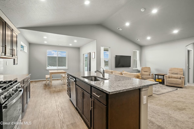 kitchen featuring dark brown cabinetry, lofted ceiling, light stone countertops, stainless steel appliances, and a sink