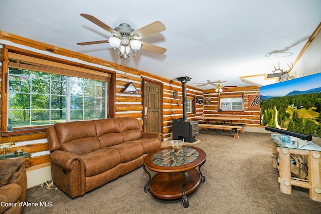 living room with ceiling fan, rustic walls, carpet flooring, and a wood stove