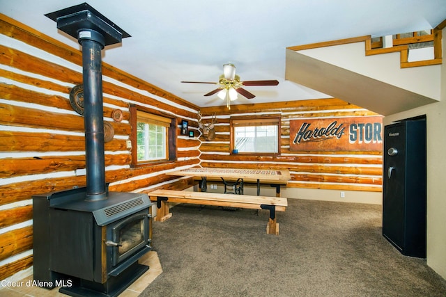 recreation room featuring a wealth of natural light, rustic walls, a wood stove, and a ceiling fan