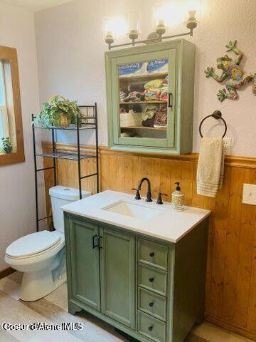 half bath with toilet, wood walls, wood finished floors, vanity, and wainscoting