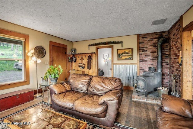 living room with a wood stove, visible vents, a textured ceiling, and wood finished floors