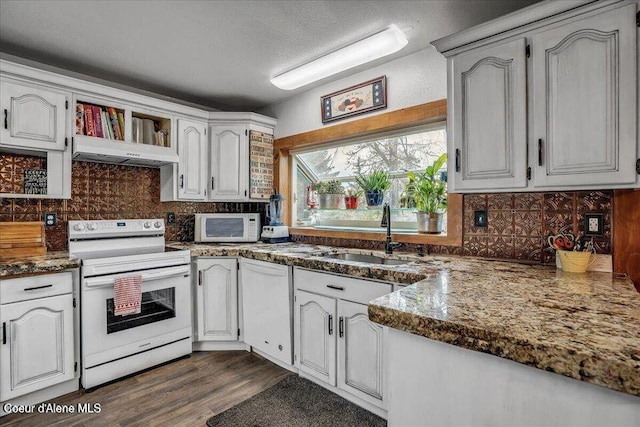 kitchen featuring under cabinet range hood, white appliances, a sink, tasteful backsplash, and dark wood finished floors