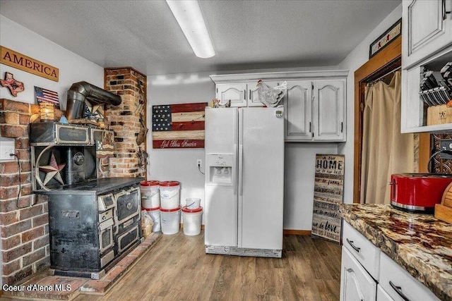 kitchen featuring white refrigerator with ice dispenser, white cabinetry, a textured ceiling, dark stone countertops, and wood finished floors