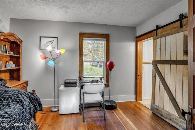 bedroom featuring hardwood / wood-style flooring, a textured ceiling, baseboards, and a barn door