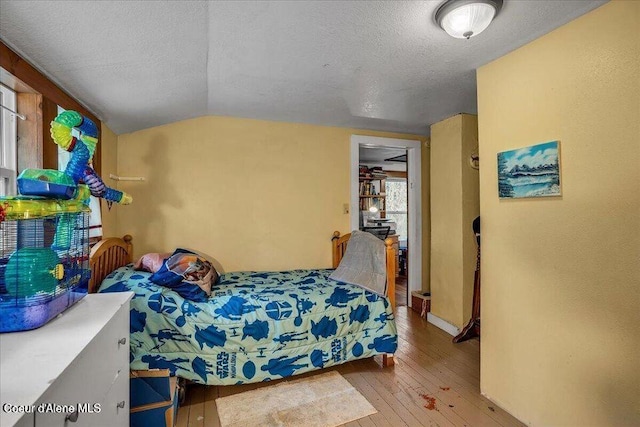 bedroom with lofted ceiling, wood-type flooring, and a textured ceiling