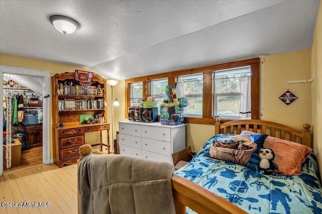 bedroom with lofted ceiling, a spacious closet, a textured ceiling, and light wood-style floors