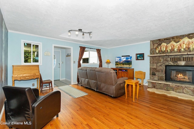 living area featuring a textured ceiling, a stone fireplace, ornamental molding, and light wood-style floors