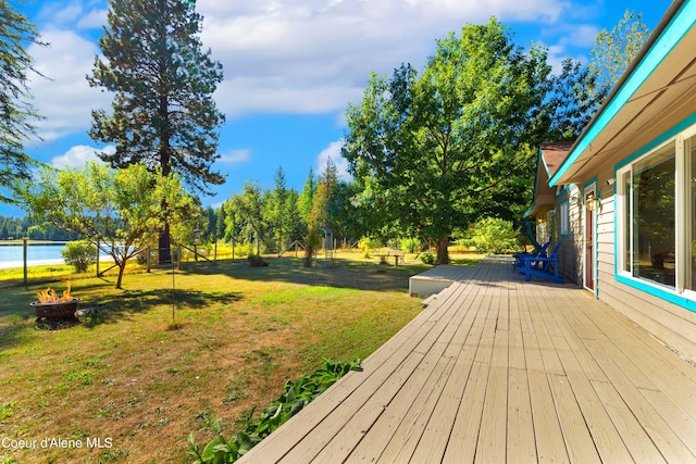 wooden deck with a water view, a yard, and a fire pit