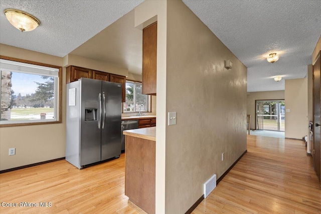 kitchen with stainless steel appliances, a sink, light countertops, light wood-type flooring, and plenty of natural light