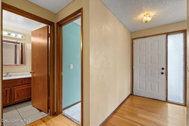 foyer entrance with a textured ceiling, light wood-type flooring, and baseboards