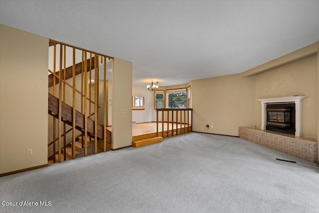 unfurnished living room with a notable chandelier, stairway, a glass covered fireplace, carpet flooring, and a textured ceiling