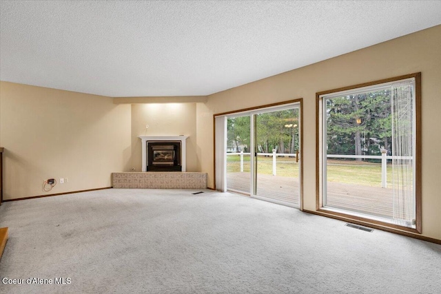 unfurnished living room with a textured ceiling, visible vents, baseboards, carpet, and a glass covered fireplace