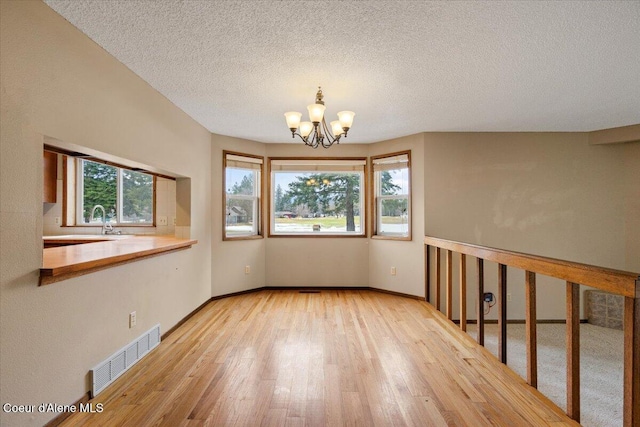 unfurnished dining area featuring visible vents, light wood-style flooring, a textured ceiling, a chandelier, and baseboards