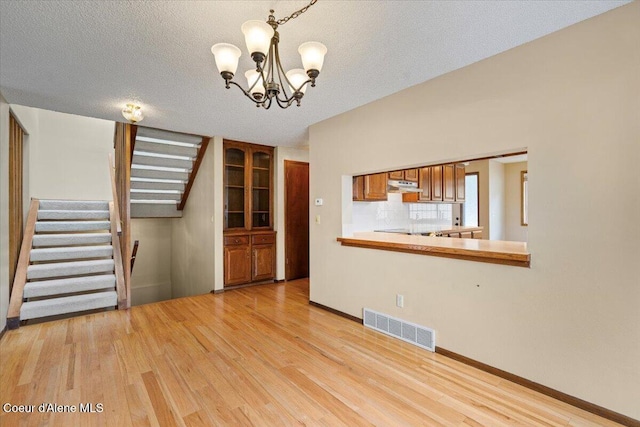 unfurnished living room featuring a notable chandelier, light wood finished floors, visible vents, a textured ceiling, and stairs