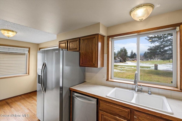 kitchen with tasteful backsplash, appliances with stainless steel finishes, light countertops, light wood-style floors, and a sink