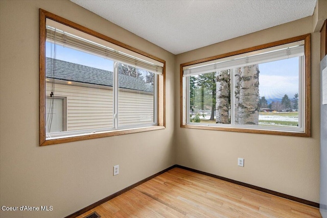 empty room with light wood finished floors, baseboards, and a textured ceiling