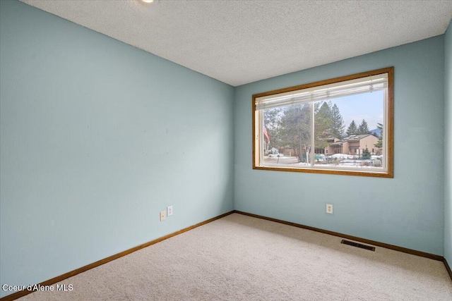 carpeted spare room with visible vents, a textured ceiling, and baseboards