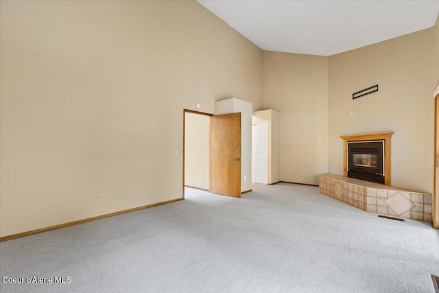 unfurnished living room with baseboards, a tile fireplace, a towering ceiling, and light colored carpet