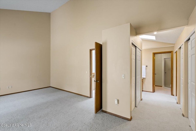 unfurnished room with light carpet, vaulted ceiling, and baseboards