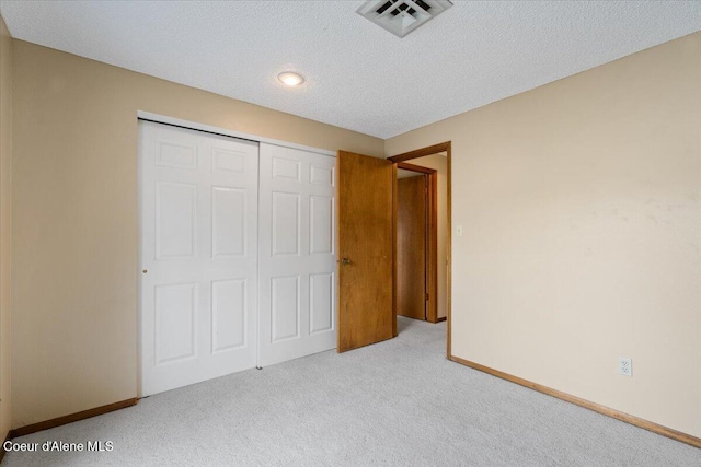 unfurnished bedroom with a closet, visible vents, carpet flooring, a textured ceiling, and baseboards