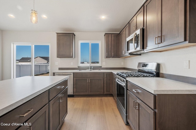 kitchen featuring light wood finished floors, appliances with stainless steel finishes, light countertops, dark brown cabinets, and a sink