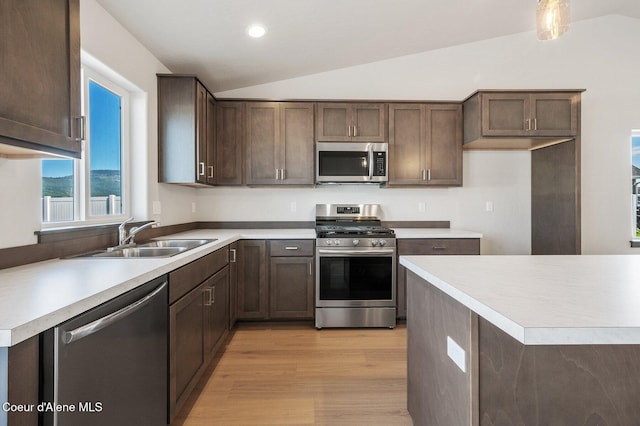 kitchen featuring stainless steel appliances, lofted ceiling, light countertops, a sink, and light wood-type flooring