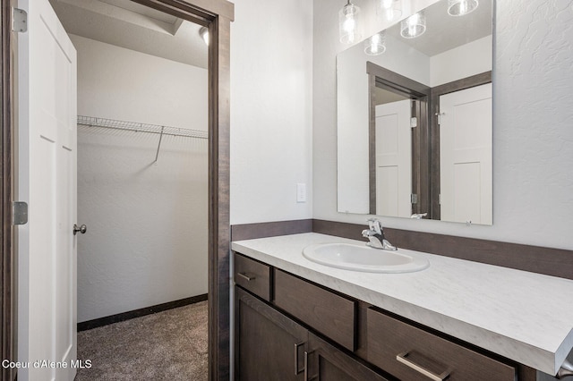 bathroom featuring a textured wall, a spacious closet, baseboards, and vanity