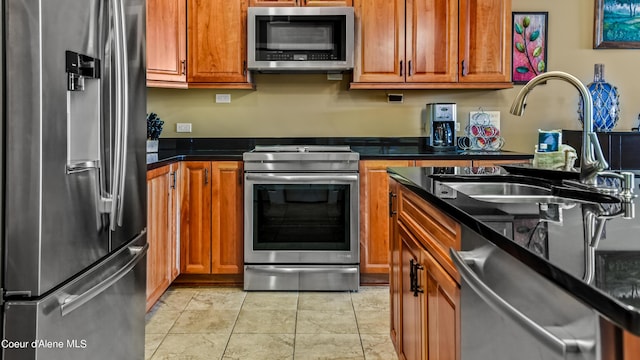 kitchen featuring appliances with stainless steel finishes, brown cabinetry, light tile patterned flooring, and a sink