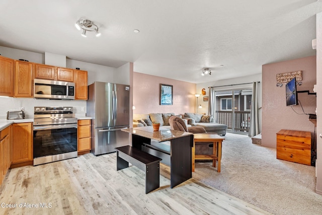 kitchen featuring a textured ceiling, light wood-style flooring, stainless steel appliances, open floor plan, and light countertops