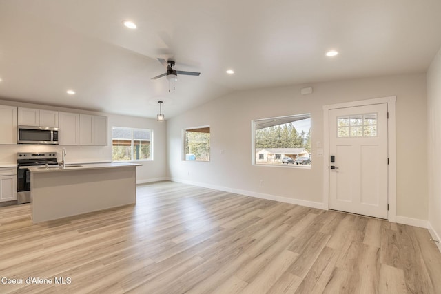 kitchen featuring lofted ceiling, stainless steel appliances, a sink, light countertops, and light wood finished floors