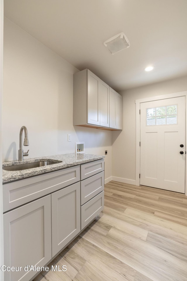 laundry area with hookup for an electric dryer, washer hookup, a sink, baseboards, and light wood-type flooring