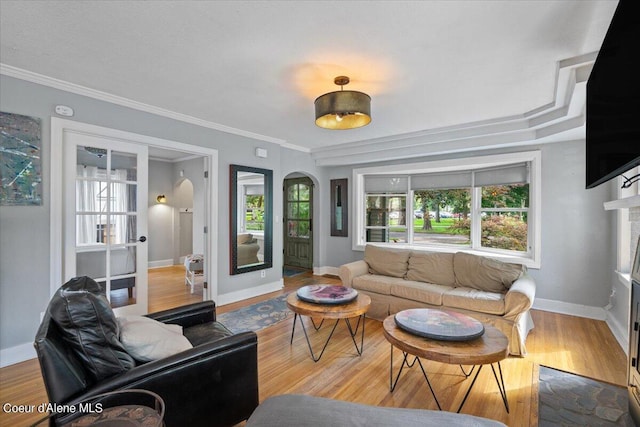 living area with a healthy amount of sunlight, arched walkways, wood finished floors, and ornamental molding