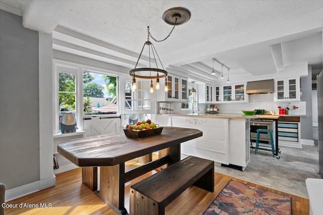 dining room featuring light wood-type flooring, a raised ceiling, a textured ceiling, and baseboards