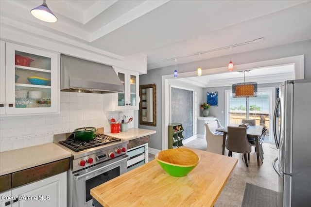 kitchen featuring white cabinets, wall chimney exhaust hood, appliances with stainless steel finishes, decorative light fixtures, and backsplash