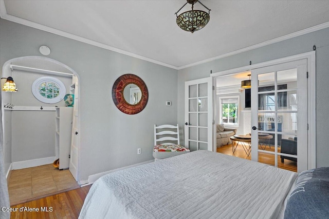 bedroom with crown molding, baseboards, wood finished floors, and french doors