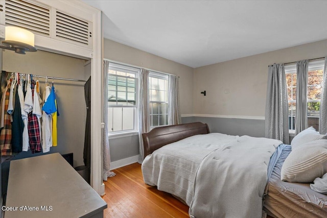 bedroom featuring a closet, multiple windows, baseboards, and wood finished floors