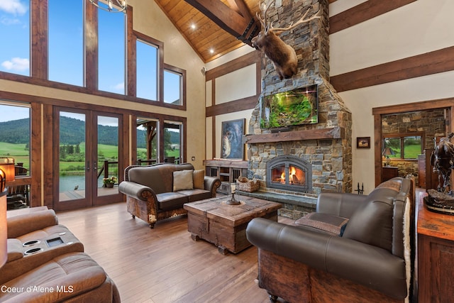 living area featuring beam ceiling, a healthy amount of sunlight, a stone fireplace, and hardwood / wood-style floors