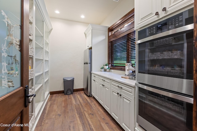 kitchen with stainless steel appliances, white cabinetry, baseboards, light countertops, and dark wood-style floors