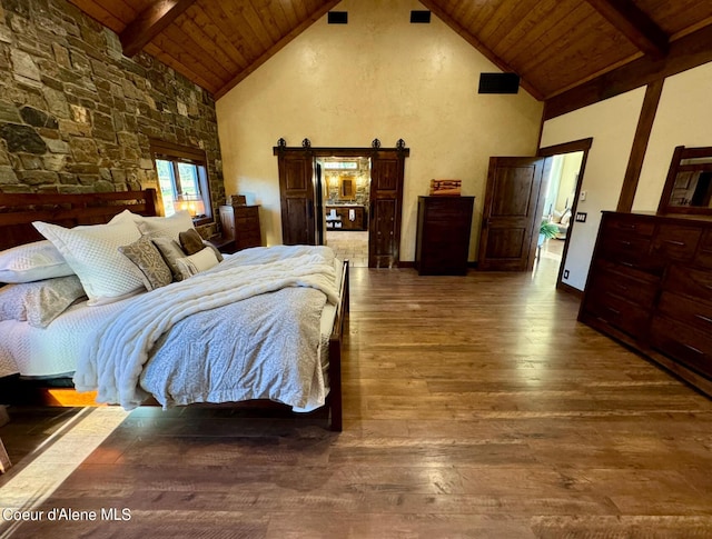 bedroom with a barn door, wooden ceiling, hardwood / wood-style floors, beamed ceiling, and high vaulted ceiling