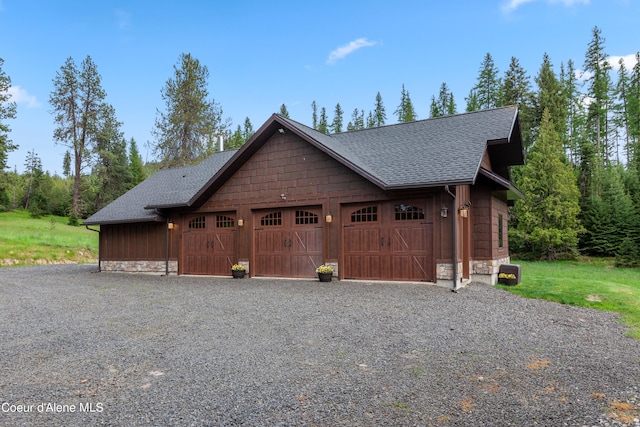 chalet / cabin with stone siding, a shingled roof, a detached garage, and board and batten siding