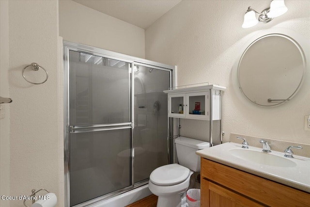 bathroom featuring a stall shower, a textured wall, vanity, and toilet