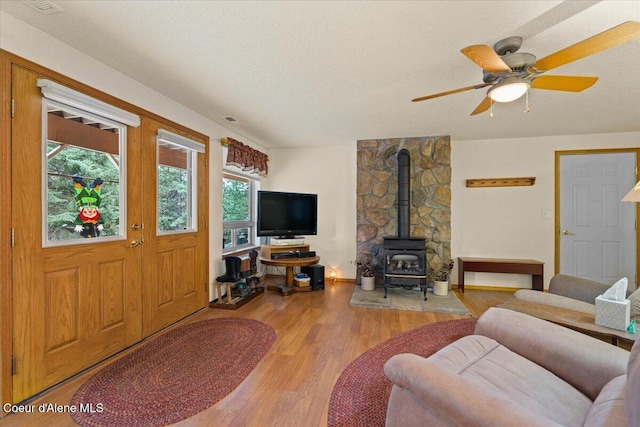 living area with light wood-type flooring, a wood stove, ceiling fan, and a textured ceiling