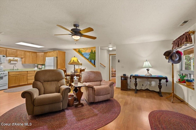 living area with a textured ceiling, ceiling fan, visible vents, and light wood-style floors