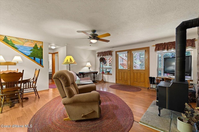 living area featuring a wood stove, visible vents, ceiling fan, and wood finished floors