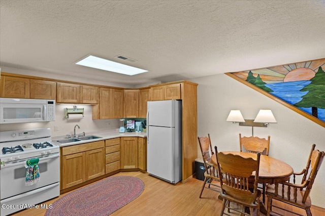 kitchen featuring light countertops, visible vents, light wood-style flooring, a sink, and white appliances