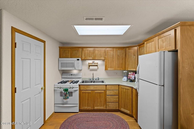 kitchen featuring light countertops, visible vents, light wood-style floors, a sink, and white appliances