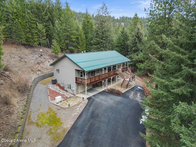 rustic home featuring metal roof, driveway, stairway, and a wooded view